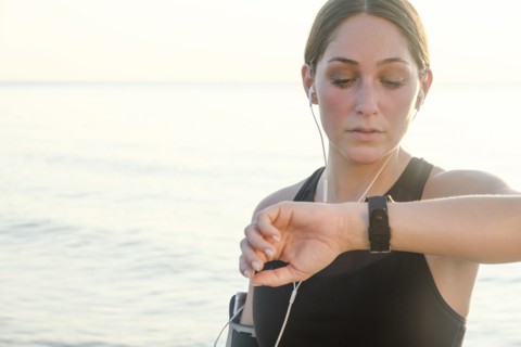 Woman wearing headphones checking wrist watch on beach