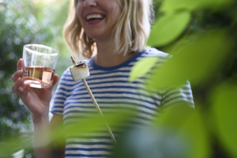 Smiling woman holding glass of wine and toasted marshmallow