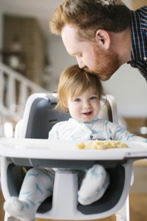 Father kissing head of his baby girl in high chair