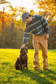 Man petting chocolate Labrador in field during autumn