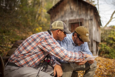 Men holding fishing rods and box by log cabin