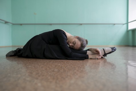Ballet dancer wearing black dress stretching in studio