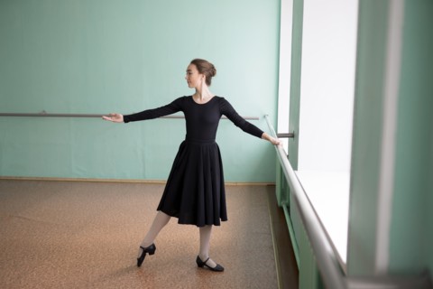 Ballet dancer wearing black dress at barre