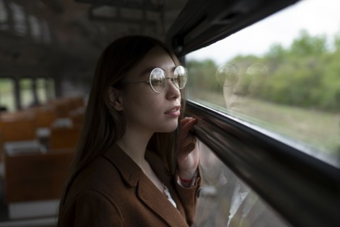 Young woman wearing glasses looking out of train window