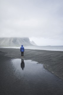 Man wearing blue coat on black sand beach in Kirkjubµjarklaustur