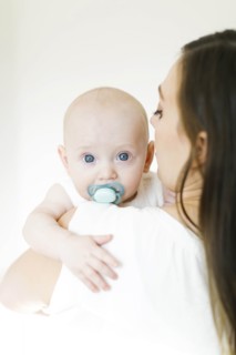Baby boy using pacifier looking over his mother's shoulder
