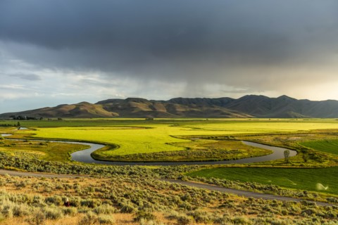 River through fields by hills in Picabo, Idaho, USA