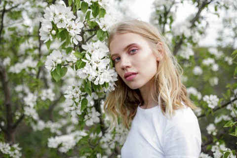 Blond haired young woman among white blossoms