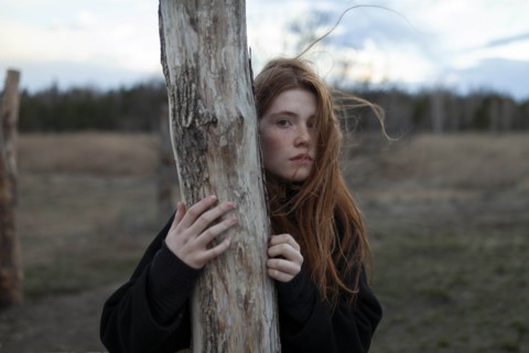 Windswept teenage girl by tree trunk