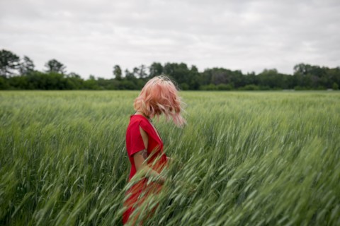 Woman with pink hair wearing red dress in wheat field