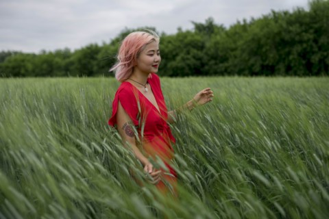 Woman with pink hair wearing red dress in wheat field