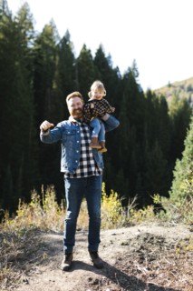 Father carrying his daughter on his shoulders by forest