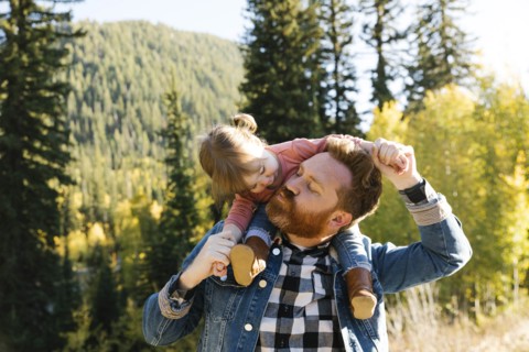 Father carrying his daughter on his shoulders by forest