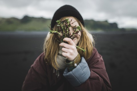 Woman holding plants over her face on beach