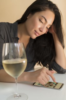 Woman using smart phone next to glass of wine