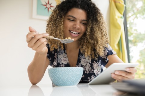 Smiling woman using tablet while eating breakfast
