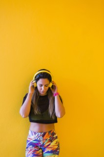 Woman wearing headphones by yellow wall