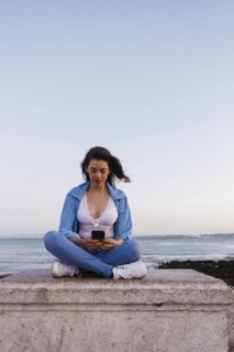 Woman using phone sitting on wall