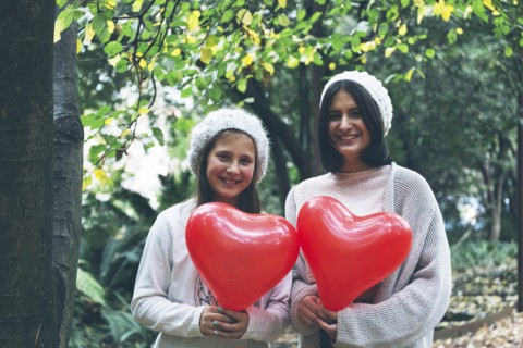 Smiling girls holding heart balloon by trees