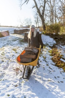 Woman holding wheelbarrow with logs in snow