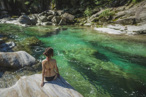 Woman wearing bikini sitting on rock by river