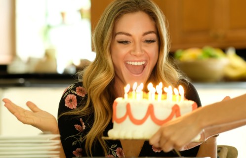Surprised young woman receiving birthday cake