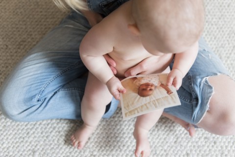 Baby girl holding photograph in her mother's lap