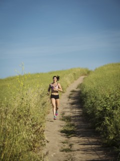 Mid adult woman jogging on path through field