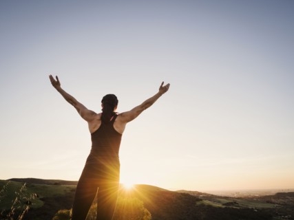 Rear view of woman with arms raised at sunset