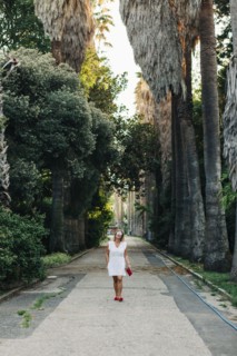 Woman in white dress walking on footpath between palm trees