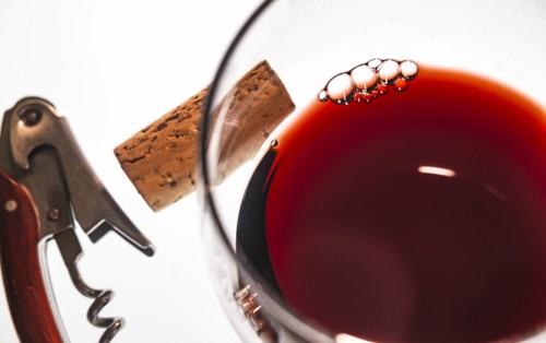 Glass of red wine with corkscrew and cork