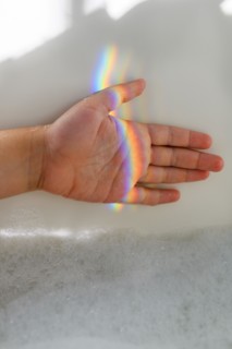 Girl's hand in rainbow light beam in bubble bath