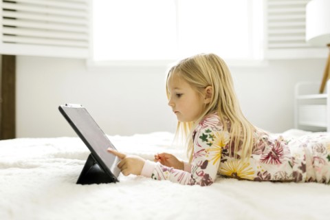 Girl in pajamas using digital tablet while lying on bed
