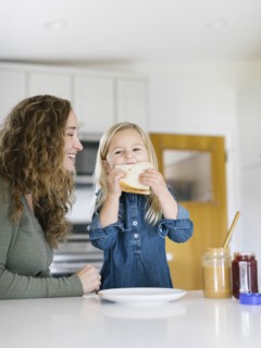 Smiling woman watching daughter eat sandwich