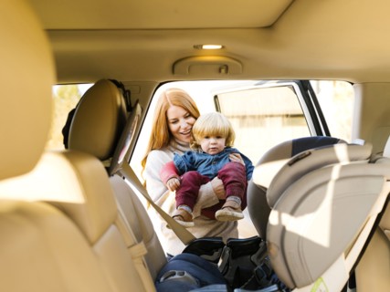 Smiling woman carrying son into car seat