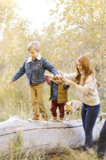 Woman holding hands of her sons as they walk on fallen tree