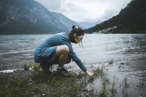 young woman crouching by lake