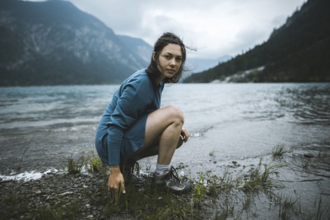 young woman crouching by lake
