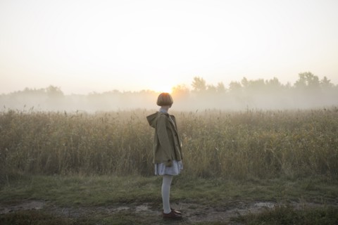 young woman by field of long grass at sunset