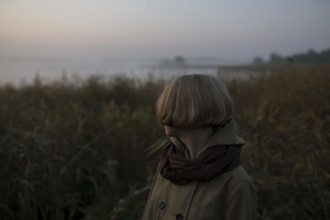 young woman in field by lake at sunset