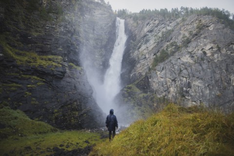young man standing on hill by waterfall