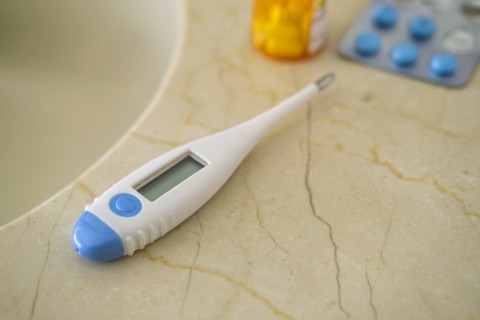 Thermometer and pills on stone surface