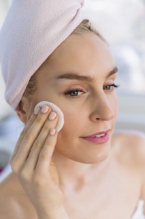 Woman cleaning face with cotton pad