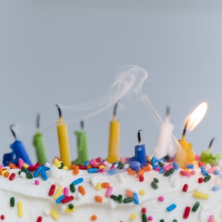 Extinguished birthday candles on cake - one still burning