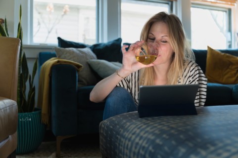 Woman drinking wine and looking at tablet at home