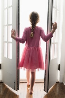 Rear view of girl (6-7) walking through doorway into light