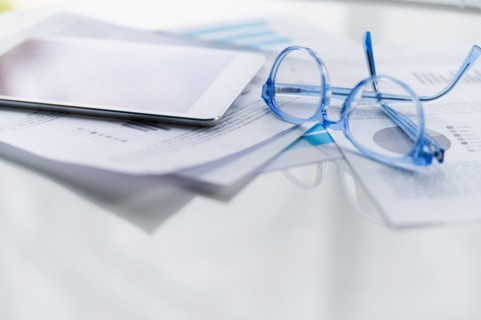 Blue eyeglasses and tablet on business papers