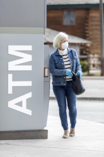 Woman wearing gloves and mask to prevent coronavirus transmission at ATM machine