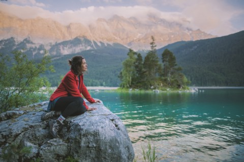 Germany, Bavaria, Eibsee, Young woman sitting on rock and looking at scenic view by Eibsee lake in Bavarian Alps