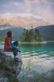 Germany, Bavaria, Eibsee, Young woman sitting on rock and looking at scenic view by Eibsee lake in Bavarian Alps